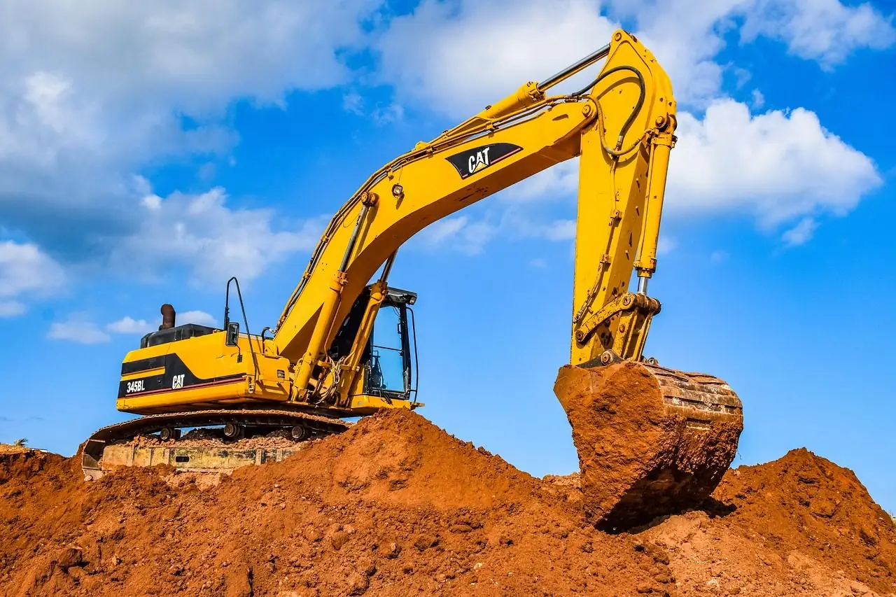 Yellow excavator digging into a mound of red earth under a blue sky