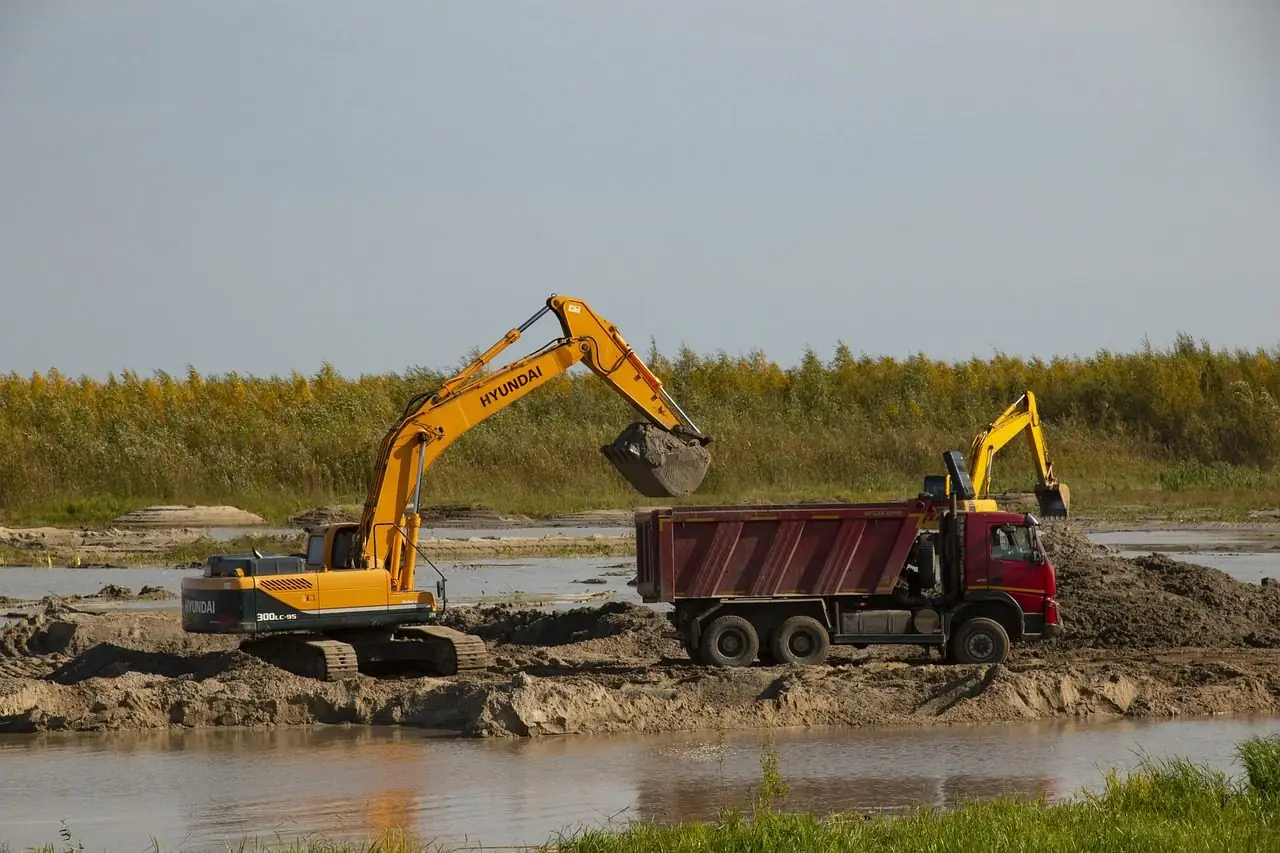 Excavator loading a dump truck at the edge of water