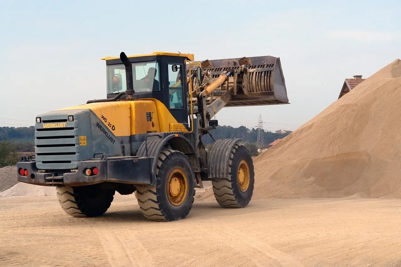 Yellow wheel loader beside a large pile of sand
