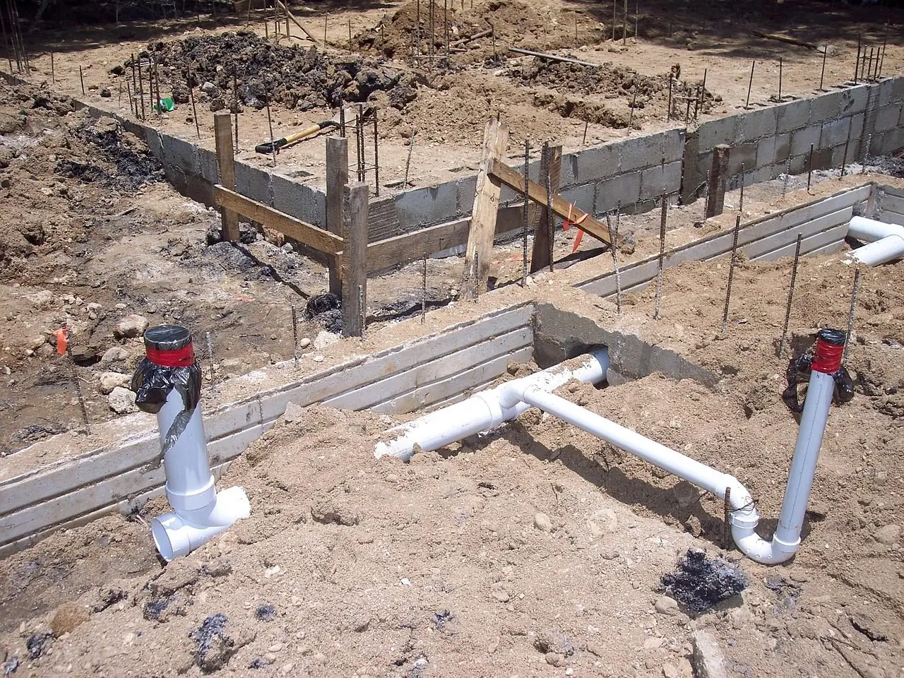 White PVC pipes set in sandy ground between block foundation walls